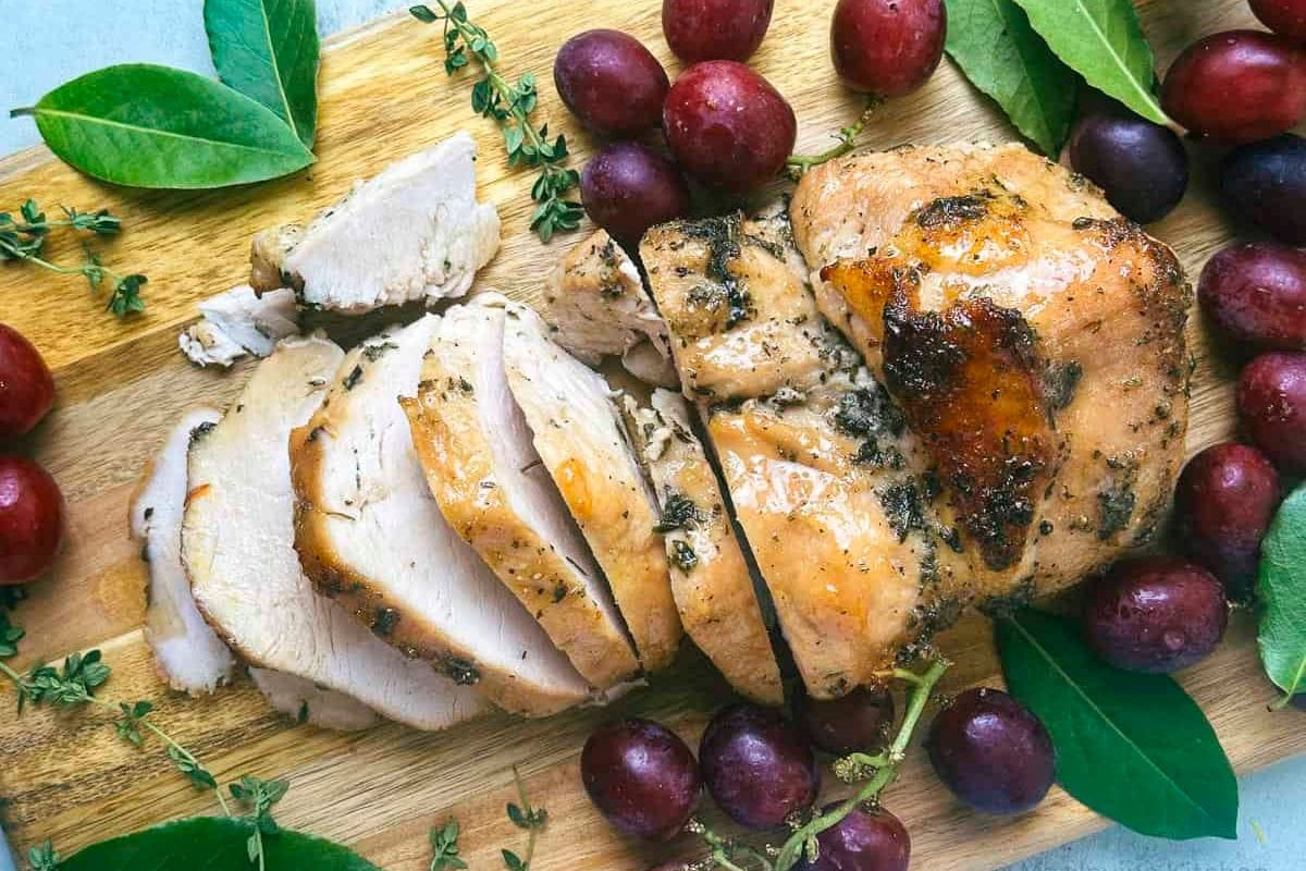 Sliced roasted turkey breast on a wooden board, surrounded by grapes and green leaves.