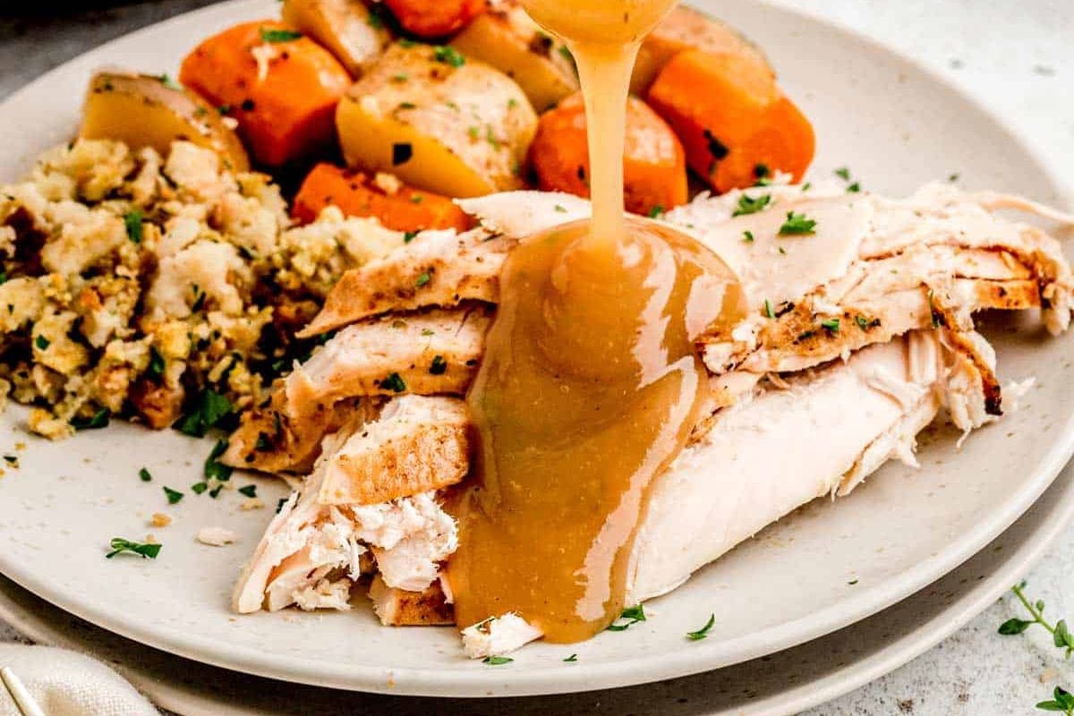 Sliced turkey with gravy, stuffing, and roasted potatoes and carrots on a plate—a perfect addition to your Thanksgiving menu ideas.