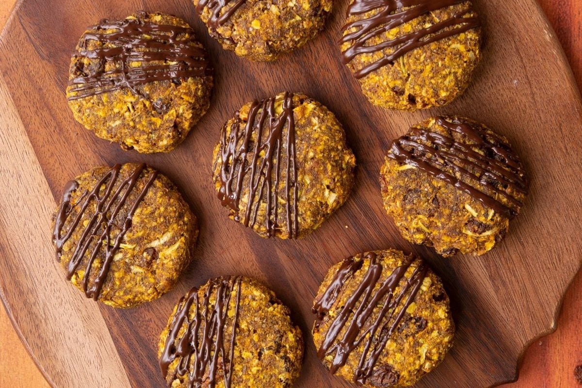 Eight cookies with a drizzle of chocolate arranged on a wooden platter.