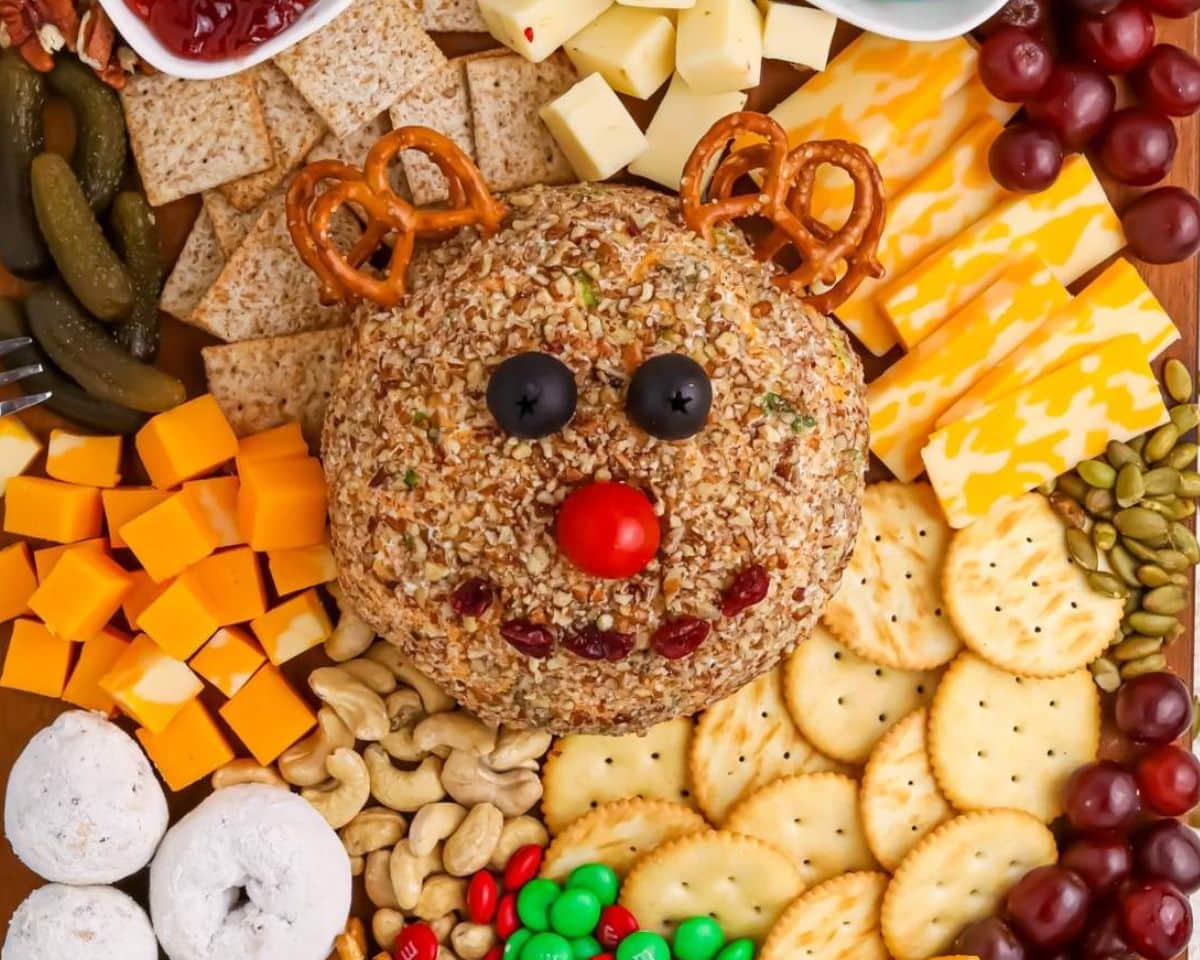 A delightful holiday recipe, this festive cheese ball is shaped like a reindeer and surrounded by crackers, cubed cheese, pretzels, grapes, and nuts.