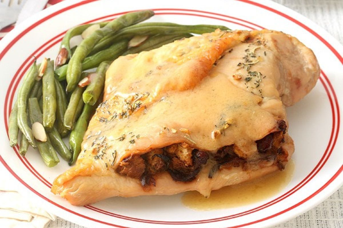 A plate with stuffed chicken breast topped with sauce, alongside steamed green beans garnished with sliced almonds.