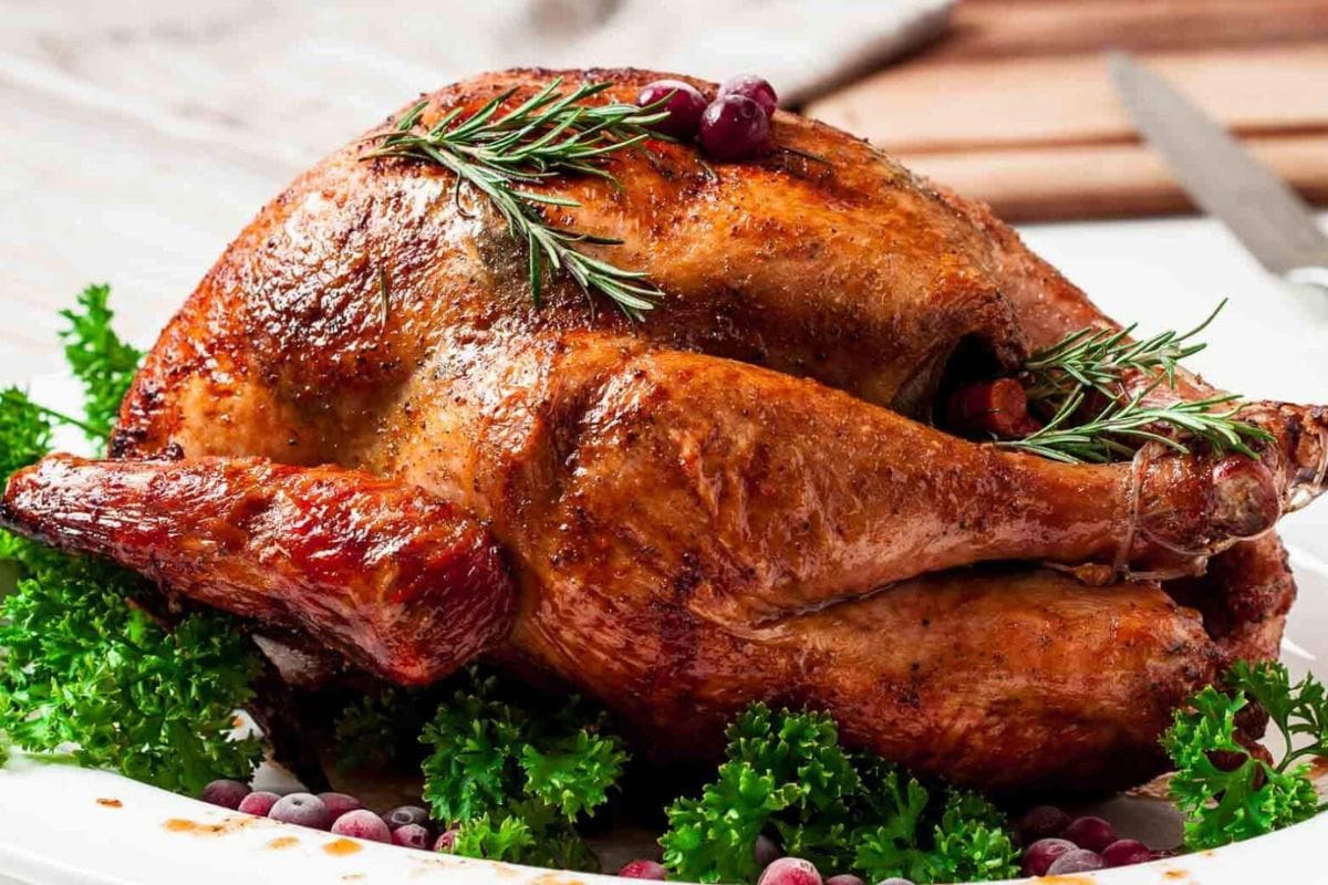 A roasted turkey, inspired by whole turkey recipes, garnished with rosemary and cranberries, surrounded by fresh parsley.