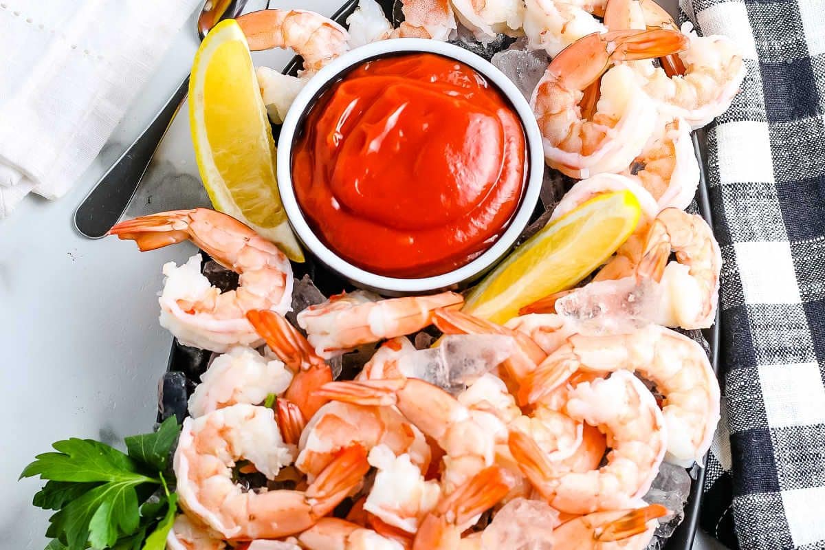Shrimp cocktail with lemon wedges, parsley, and a bowl of red sauce on a platter.