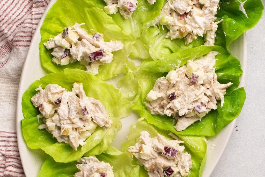 Lettuce wraps filled with chicken salad mixed with diced apples and nuts on a white plate.