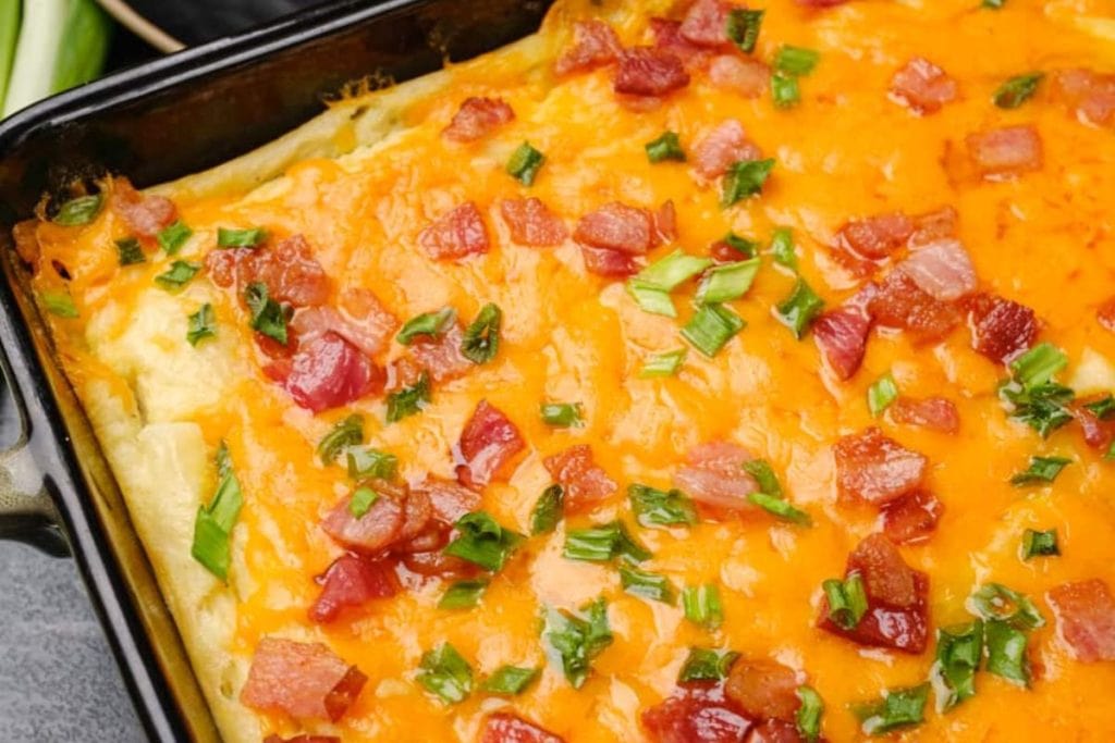 Close-up of a baked dish with melted cheese, chopped green onions, and bacon bits in a black pan.