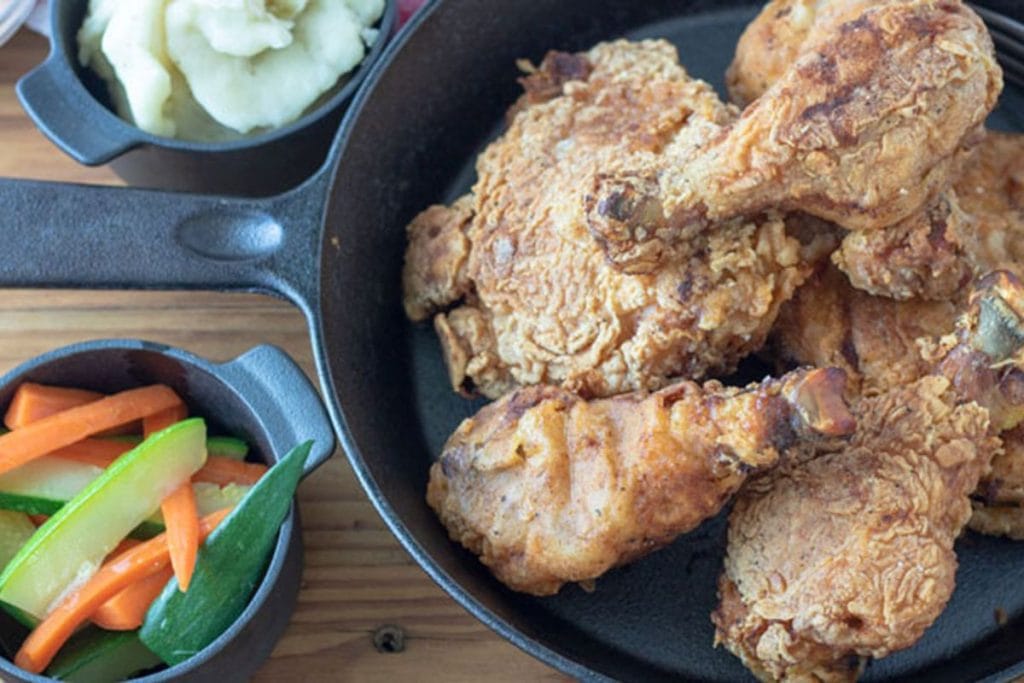 Fried chicken pieces sizzle in a cast iron skillet, creating a 5 Star Soul Food experience, accompanied by creamy mashed potatoes and vibrant mixed vegetables on the side.