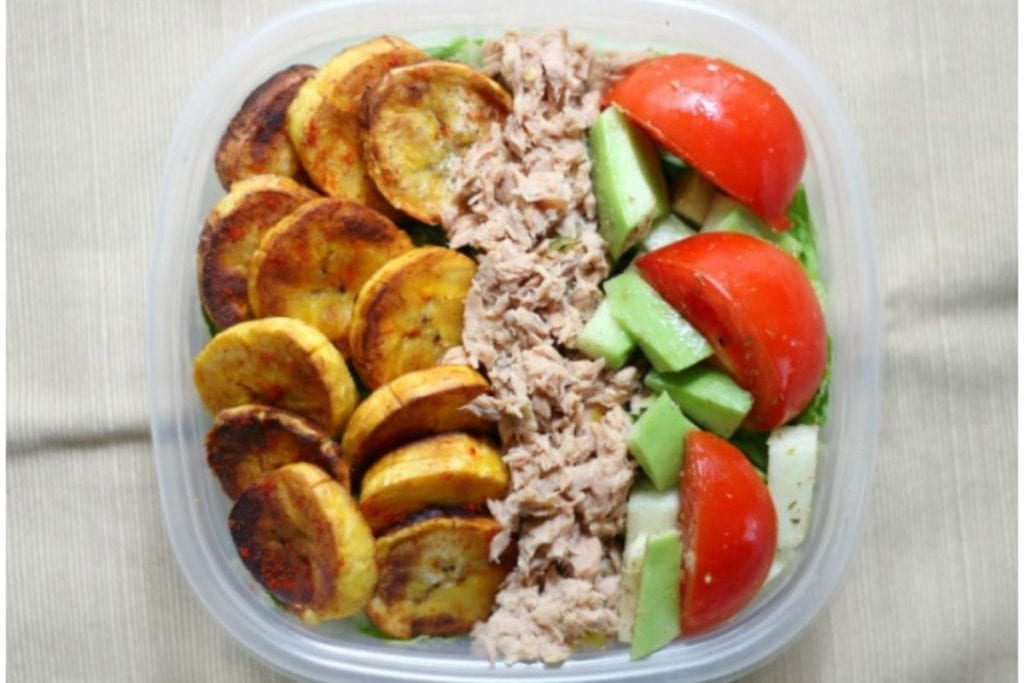 A container filled with fried plantain slices, shredded tuna, avocado slices, and tomato wedges.