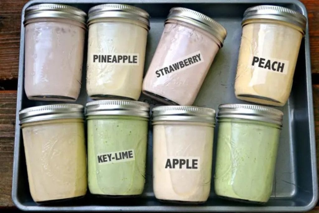 Eight jars with metal lids labeled with flavors: Pineapple, Strawberry, Peach, Key-Lime, and Apple, arranged on a metal tray.