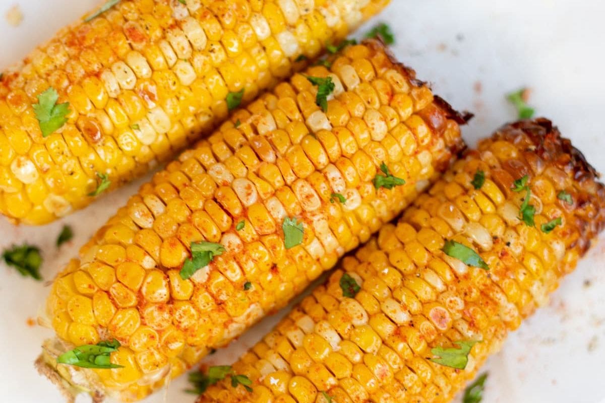 Three grilled corncobs, seasoned with spices and garnished with chopped herbs, make for the perfect football game food on a crisp white background.