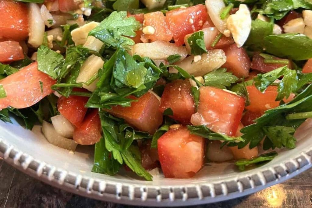 A close-up of a bowl of salad showcases vibrant chopped tomatoes, onions, and parsley—an inspiring addition to your healthy salad recipes.