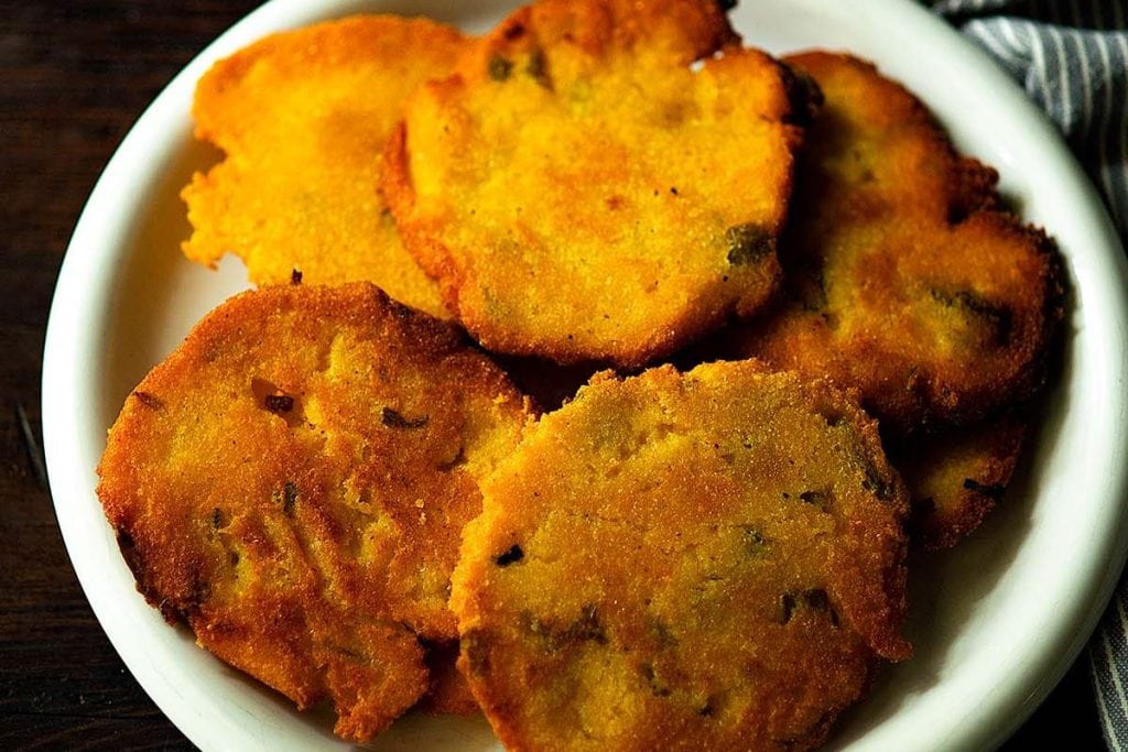 A white plate filled with a stack of crispy, golden-brown fritters, their textured edges and visible chunks making them an irresistible addition to any soul food dinner party menu.