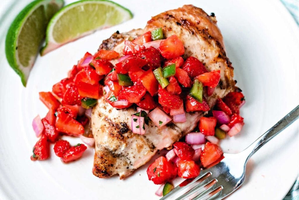 Grilled chicken breast topped with diced tomatoes, red onions, and green peppers, served with lime wedges on a white plate—a perfect example of healthy chicken recipes.