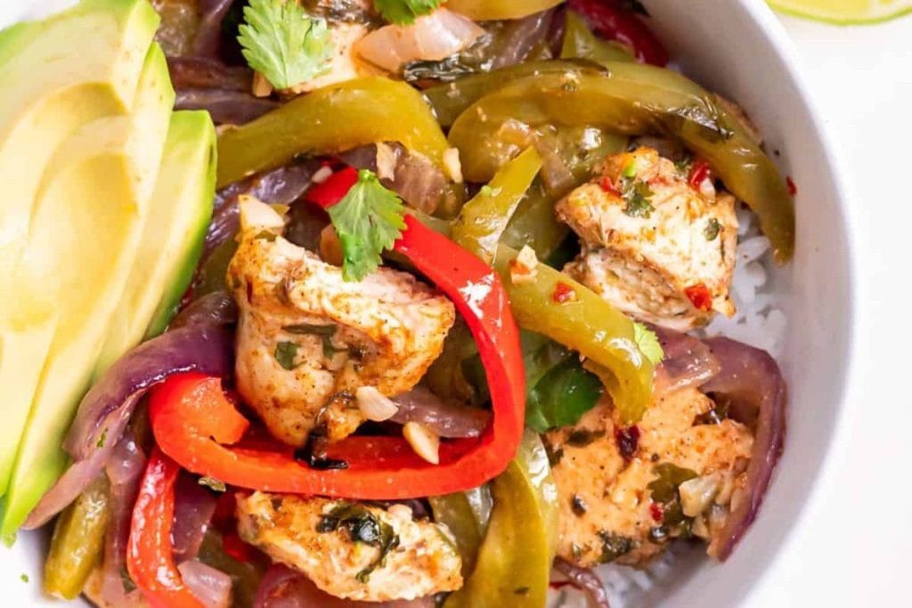 A bowl of seasoned chicken pieces with red and green bell peppers, red onions, and avocado slices, garnished with cilantro—a delicious addition to healthy chicken recipes.