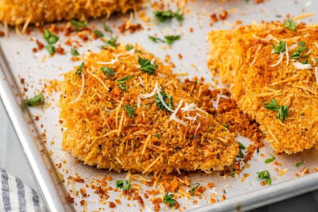 Breaded chicken pieces, part of my favorite healthy chicken recipes, are garnished with grated cheese and parsley on a baking tray.