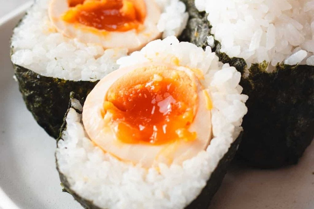 Close-up of sushi rolls wrapped in seaweed, filled with rice and a soft-boiled egg with a runny yolk, perfect for an on-the-go lunch.