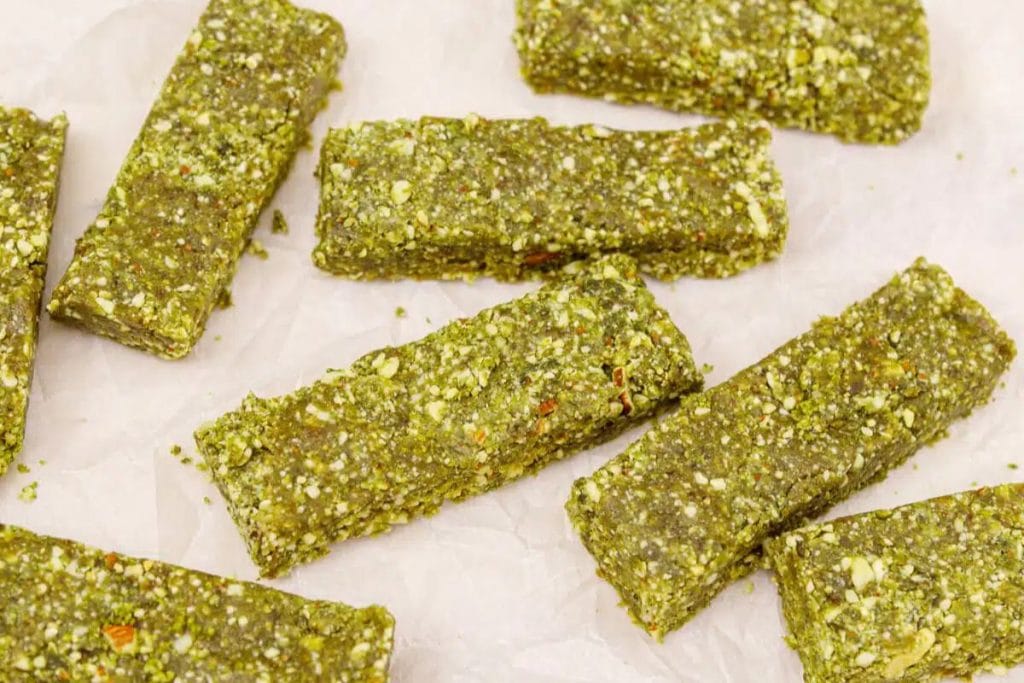 Rectangular green energy bars with visible nut and seed pieces, arranged on a sheet of parchment paper.