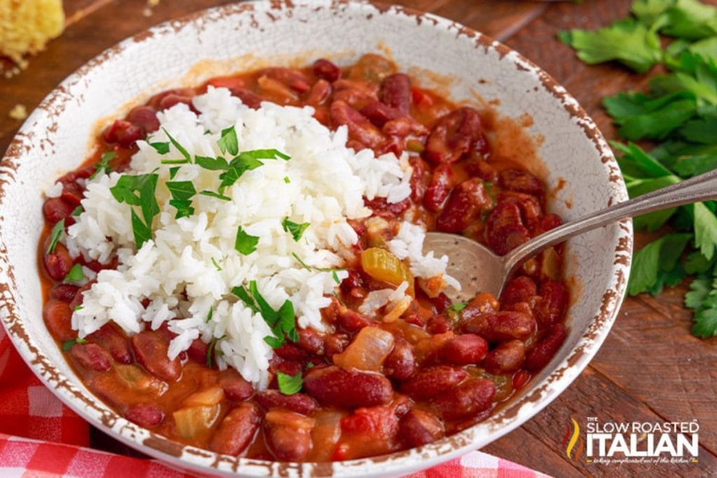 A bowl of red beans and rice, a soul food dinner classic, garnished with parsley, featuring a spoon on the side and resting atop a red checkered napkin.
