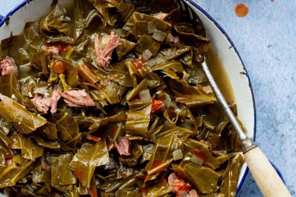 A 5 Star Soul Food delight, this dish features tender, cooked collard greens mingling with delectable chunks of meat in a bowl, invitingly paired with a spoon.