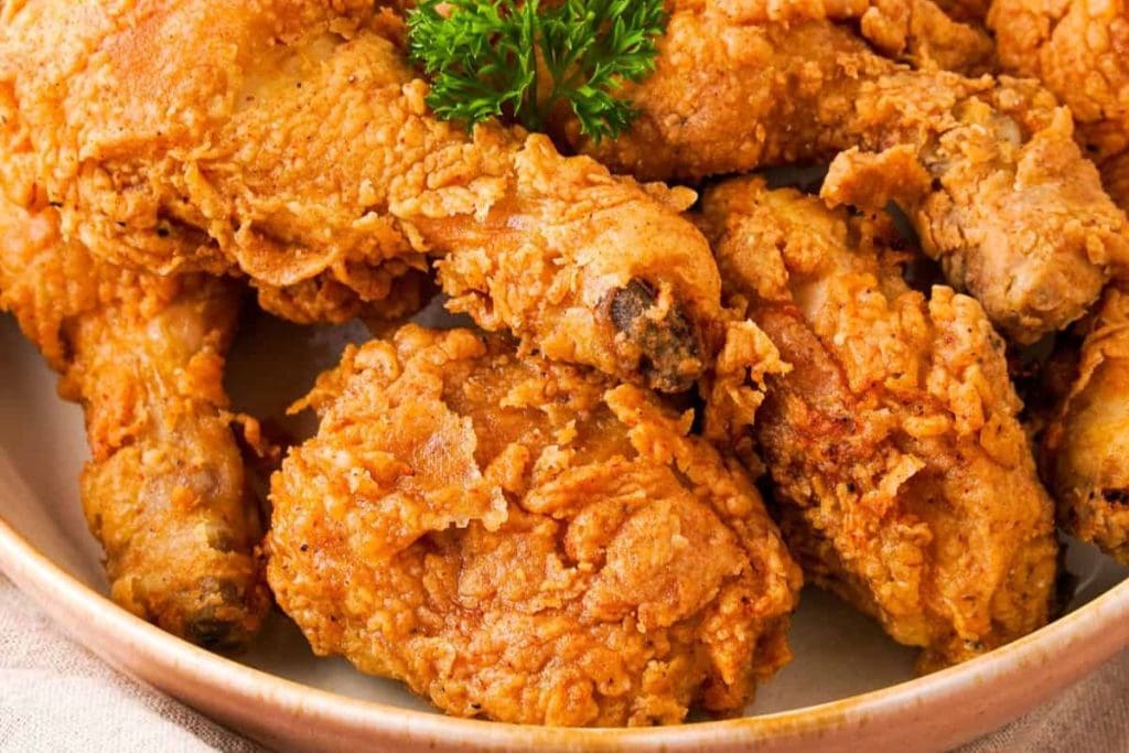 A plate full of crispy fried chicken pieces with a golden brown crust, garnished with a small sprig of parsley on top, makes the perfect centerpiece for your soul food dinner party menu.
