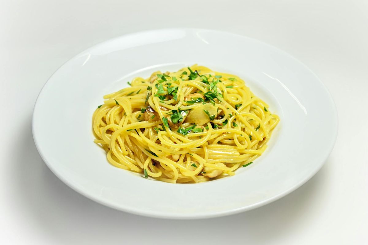 A plate of spaghetti with chopped herbs on top, served on a white plate.