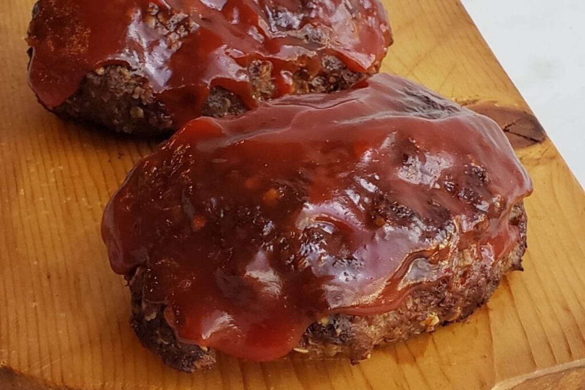 Two glazed mini meatloaves on a wooden board, perfect for February meals, coated with a glossy red sauce.