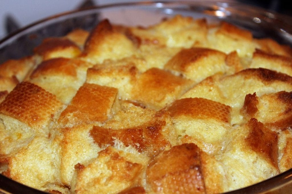Close-up of a baked bread pudding in a round glass dish, featuring golden-brown cubed bread pieces with a slightly crispy finish.