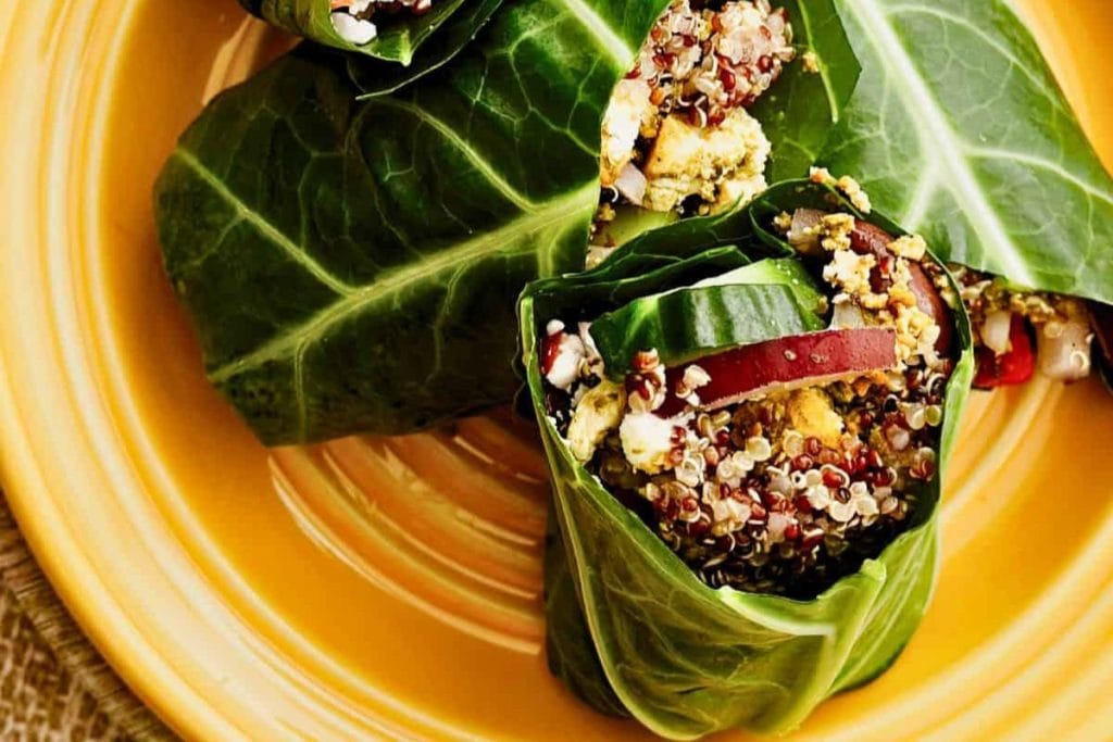 Collard green wraps filled with quinoa, sliced red apple, and crumbled cheese on a yellow plate.