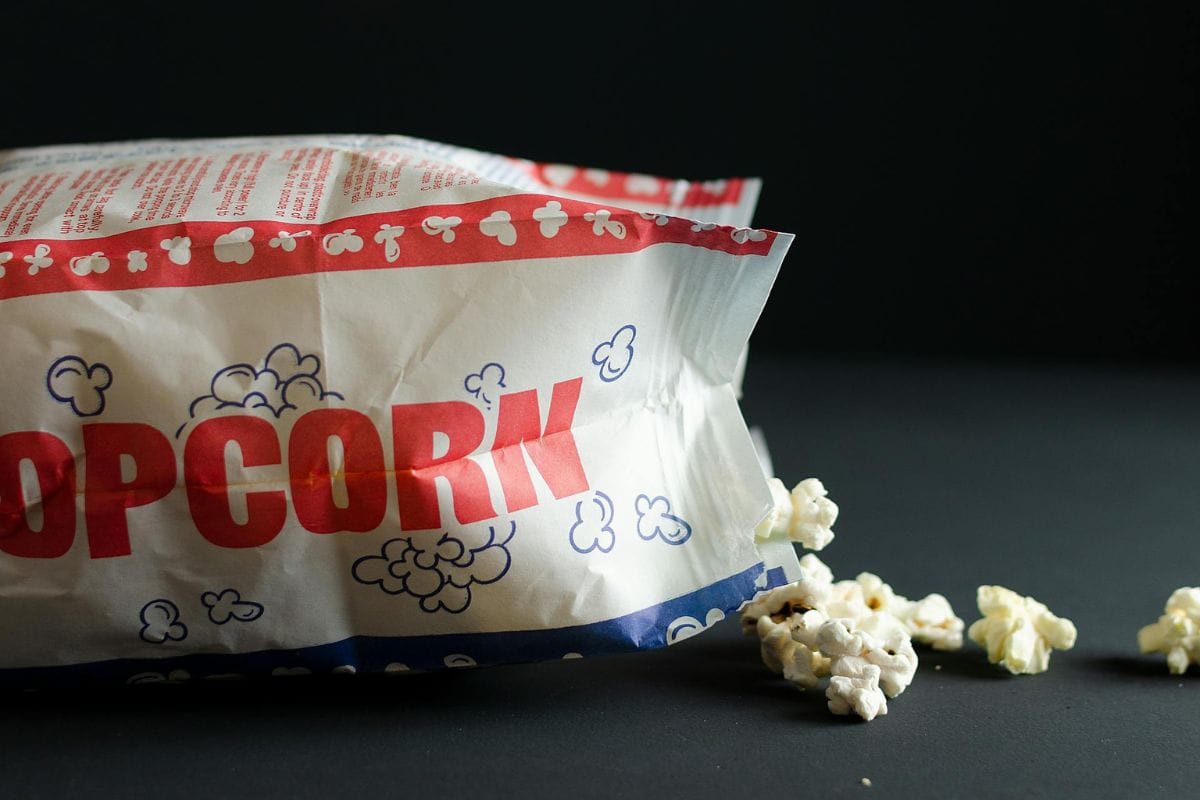 A microwave popcorn bag lies on its side with popped kernels spilling out against a dark background.