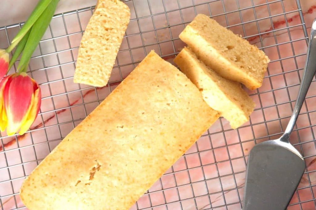 A loaf of sliced cake on a cooling rack with a serving utensil and a tulip on the side.