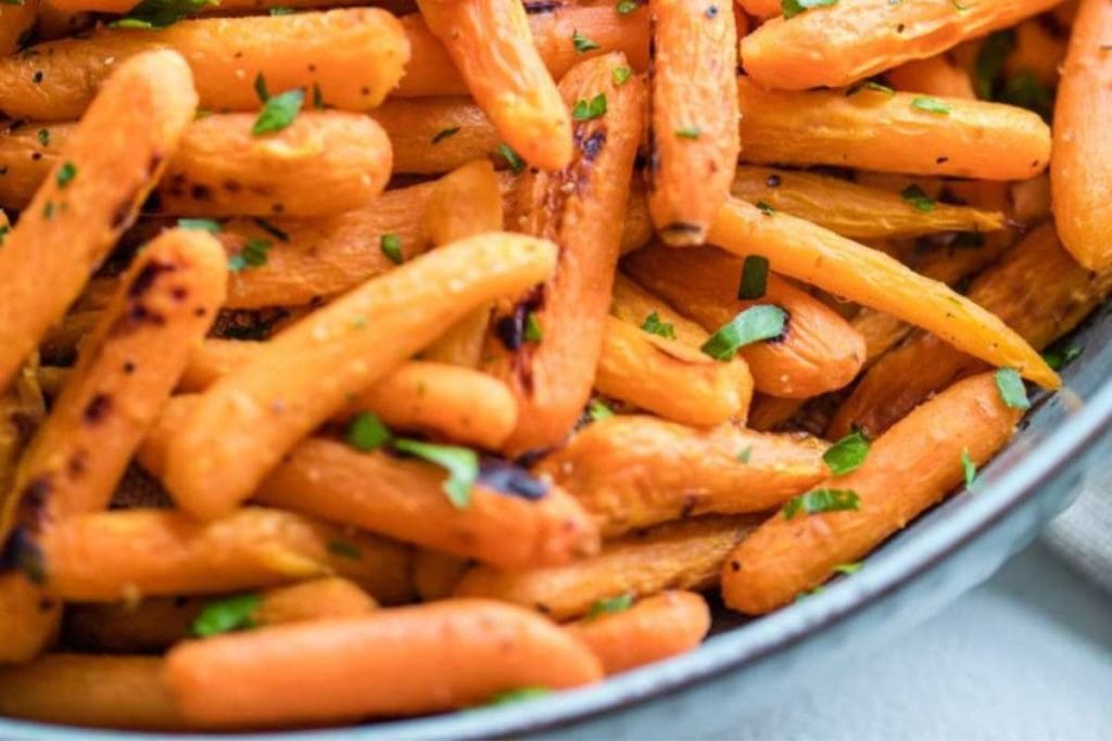 A close-up of roasted baby carrots, lightly charred and garnished with chopped green herbs.