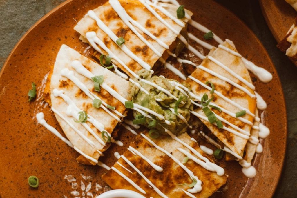 A plate of quesadillas topped with sliced green onions, a dollop of guacamole, and drizzled with a white sauce.