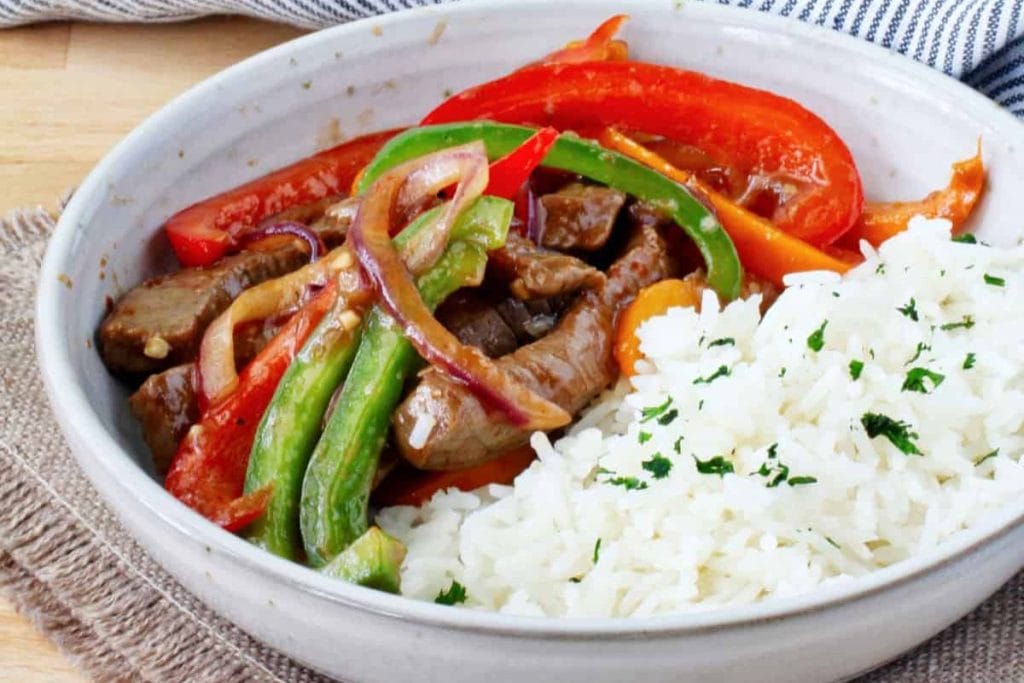 A bowl of stir-fried beef with red and green bell peppers and onions, served alongside white rice, garnished with parsley—one of the perfect recipes to make in February.