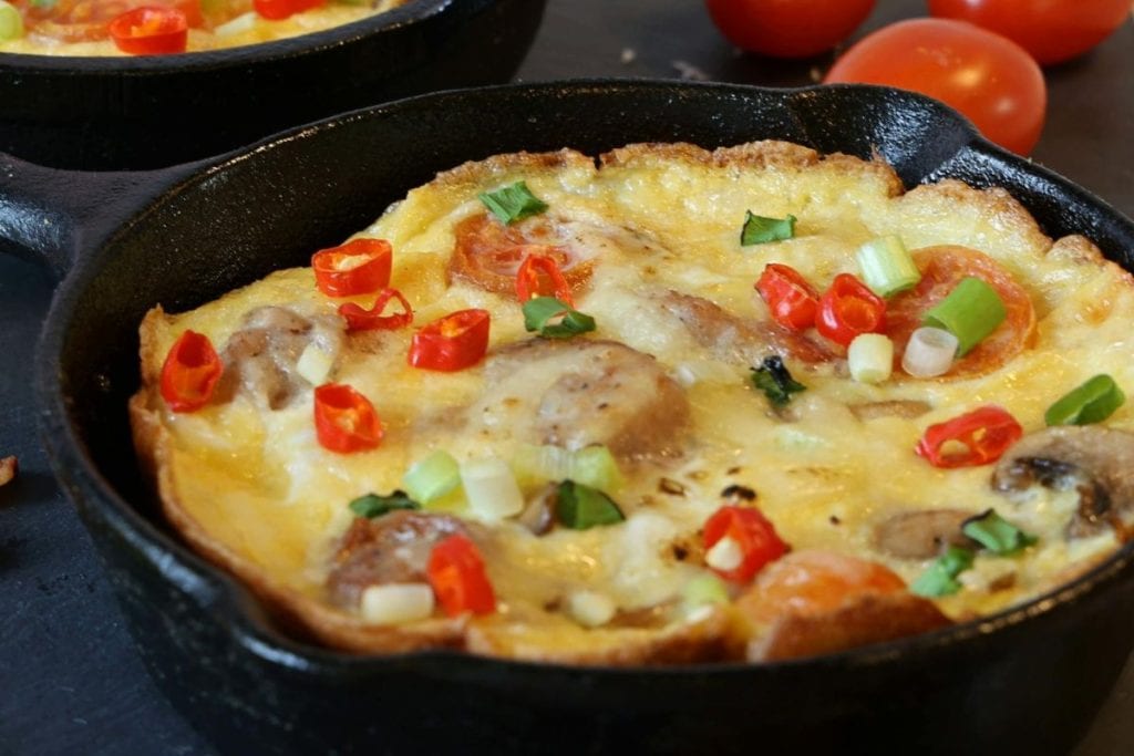 Frittata in a skillet with mushrooms, sliced red and green peppers, and scallions.