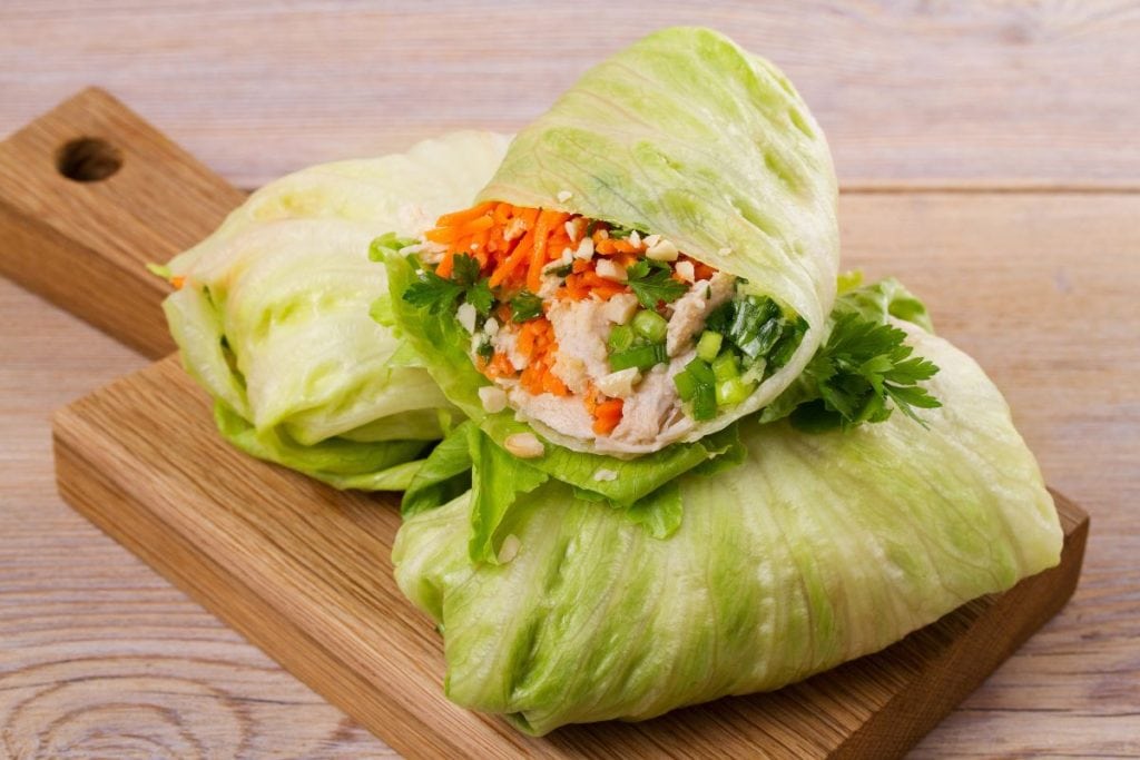 Lettuce wraps filled with chicken, carrots, and herbs on a wooden board.