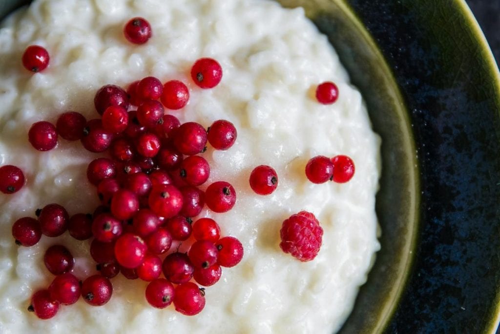 Bowl of rice pudding topped with red currants and a single raspberry on a dark background.