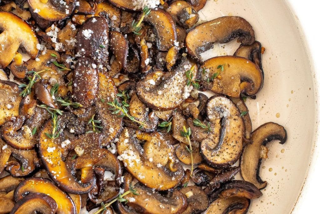 Sautéed sliced mushrooms with herbs and seasoning in a pan.