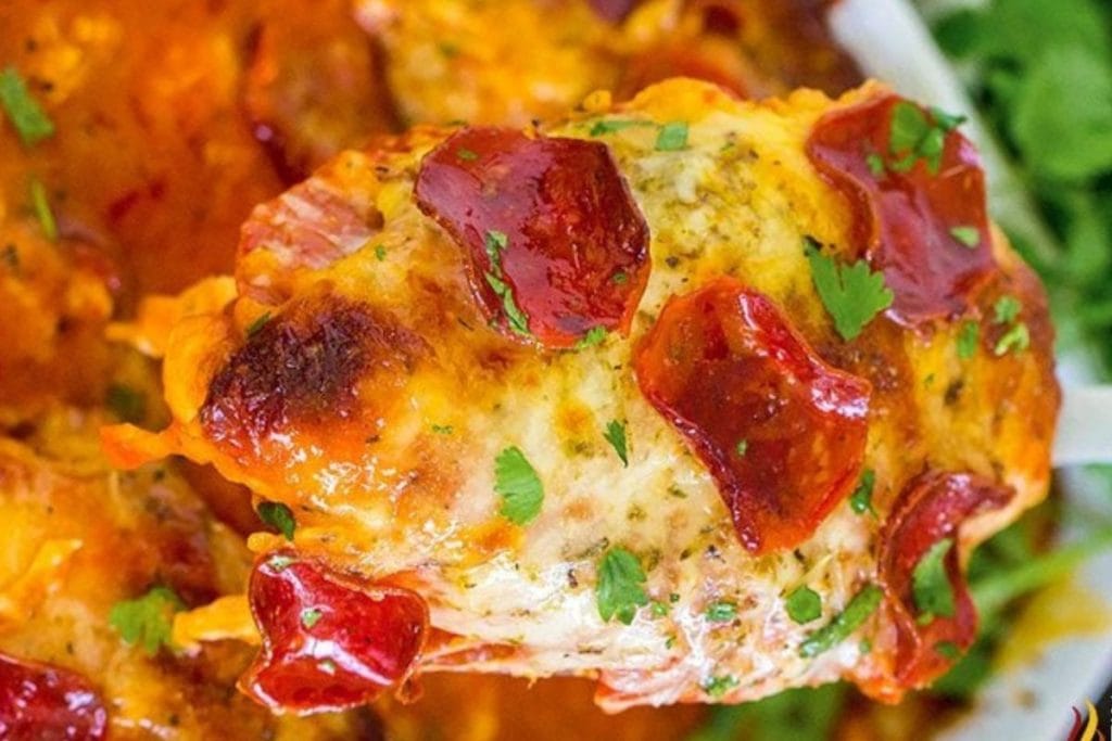 Close-up of a baked dish topped with melted cheese, pepperoni slices, and parsley on a breaded base.