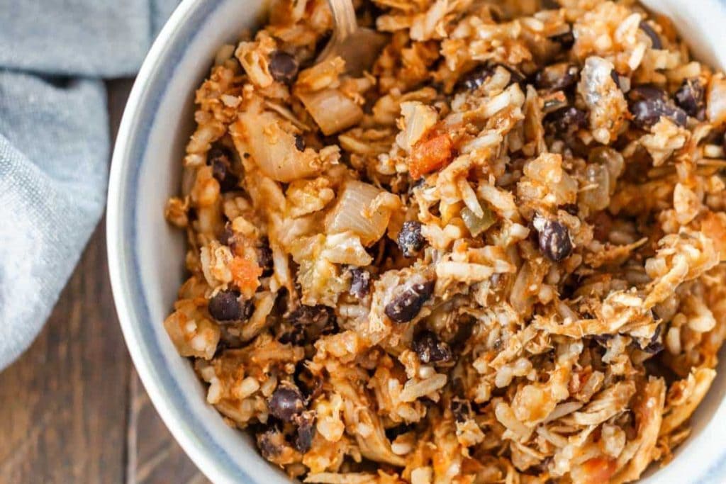 A bowl filled with a mixture of rice, shredded chicken, black beans, tomatoes, and onions.