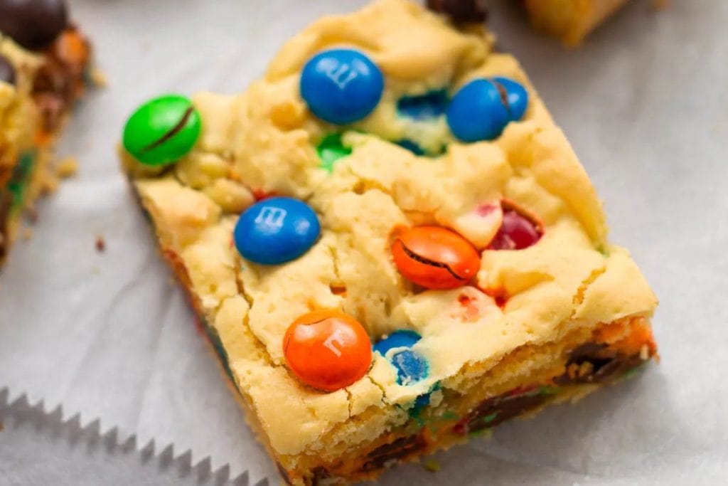 A cookie bar topped with colorful candy-coated chocolates on a piece of parchment paper.