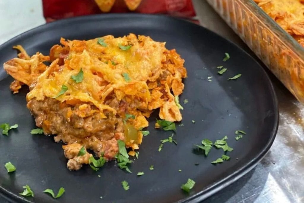 A serving of baked cheesy casserole on a black plate, topped with chopped herbs.