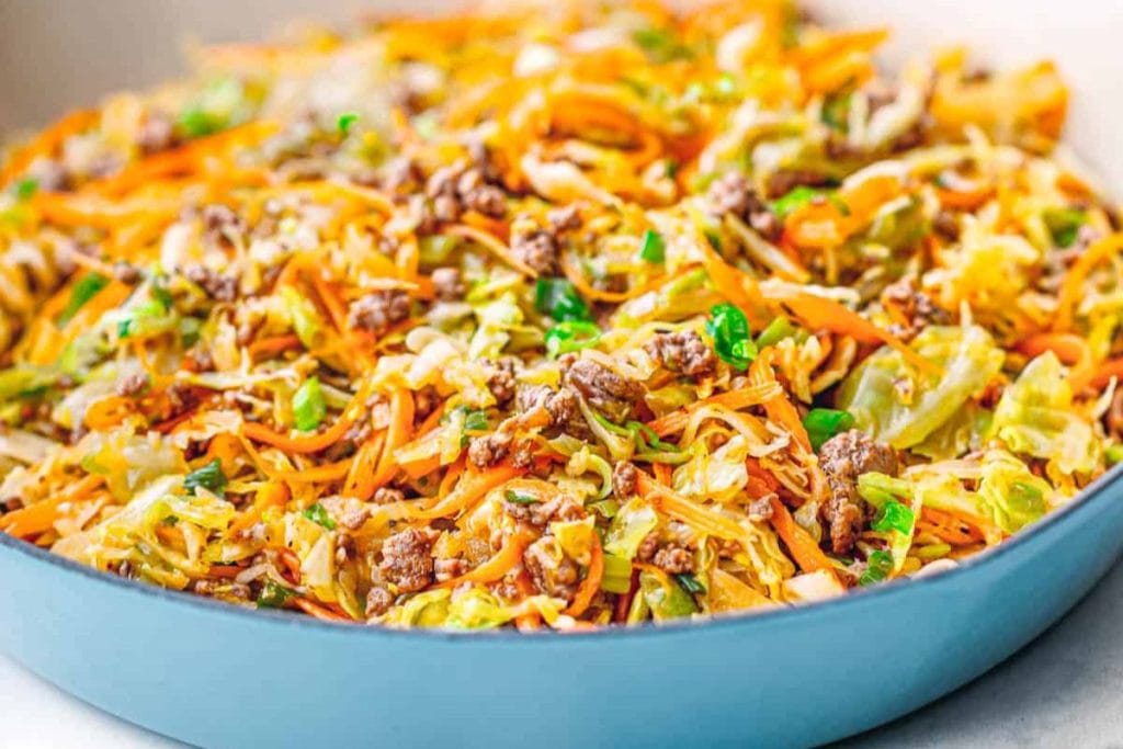 A dish filled with cooked ground meat, shredded carrots, chopped cabbage, and garnished with green onions.