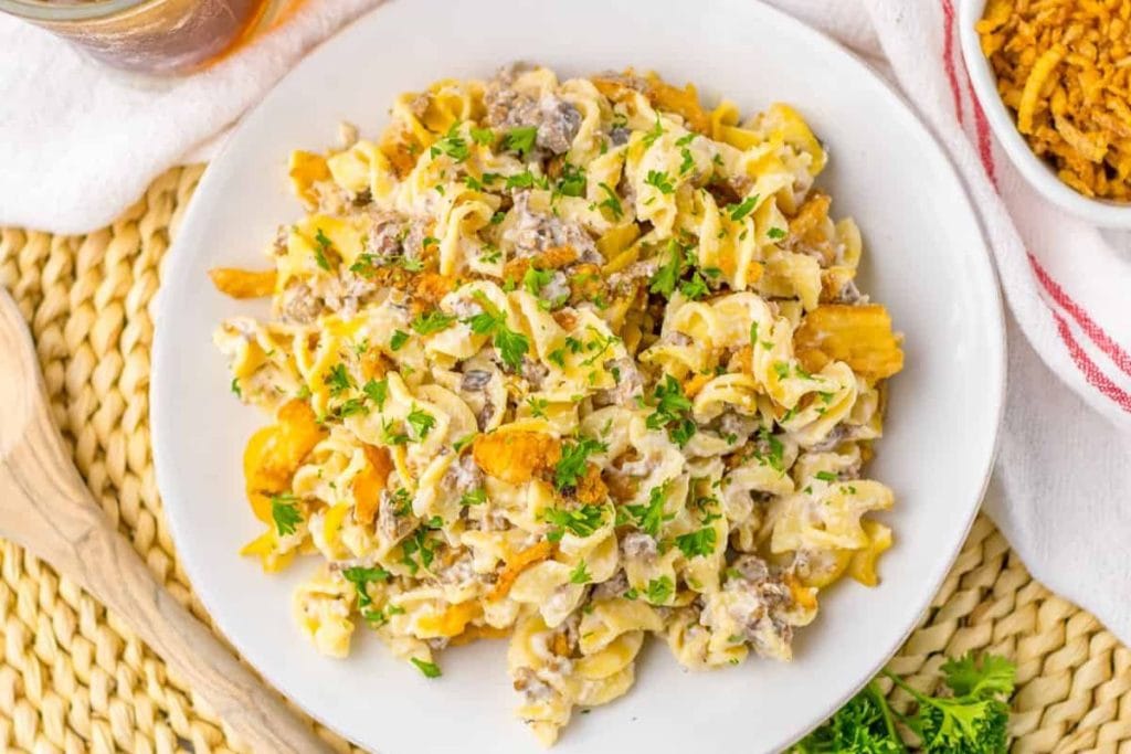 A plate of pasta salad with curly noodles, ground beef, chopped parsley, and a creamy dressing, garnished with crispy bits.