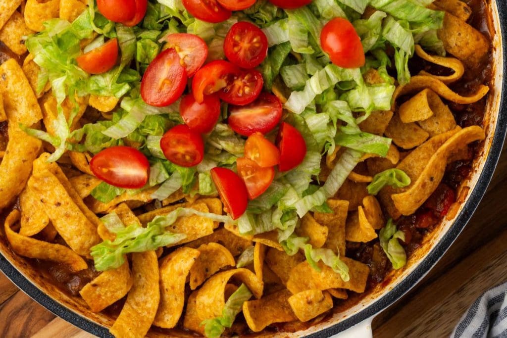 A dish with Fritos corn chips, topped with shredded lettuce and halved cherry tomatoes.