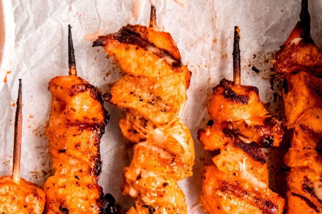Close-up of grilled chicken skewers with a golden brown crust on parchment paper.