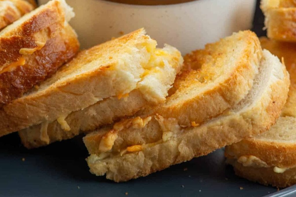 Close-up of stacked grilled cheese sandwiches with golden-brown crusts and melted cheese oozing out, set on a dark surface.