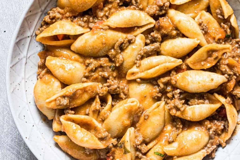 A bowl of shell pasta mixed with ground meat and a creamy sauce.