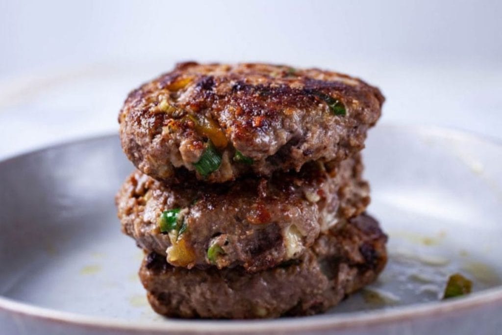 Three grilled hamburger patties stacked on a plate, garnished with herbs.