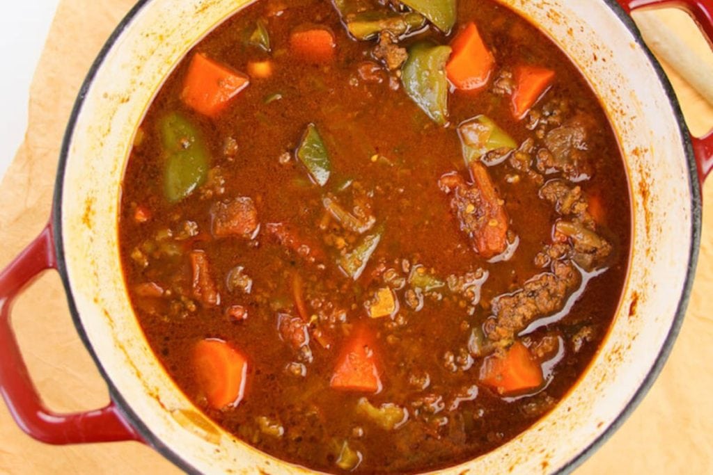 A pot of hearty beef stew with chunks of carrots, bell peppers, and other vegetables in a rich, red broth.