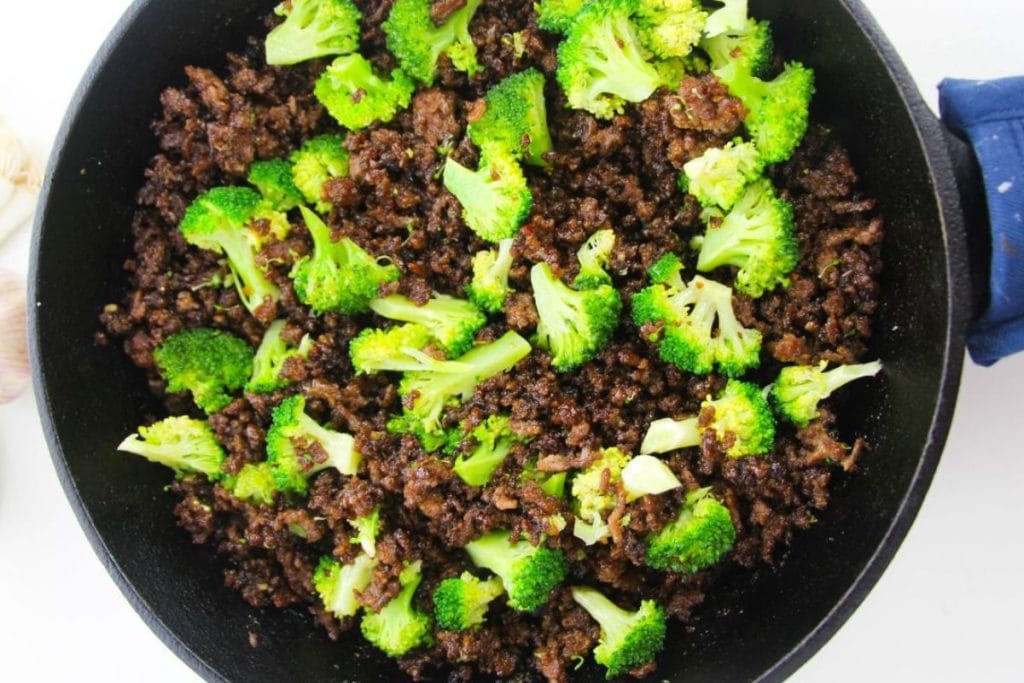 A skillet filled with cooked ground beef and bright green broccoli florets.