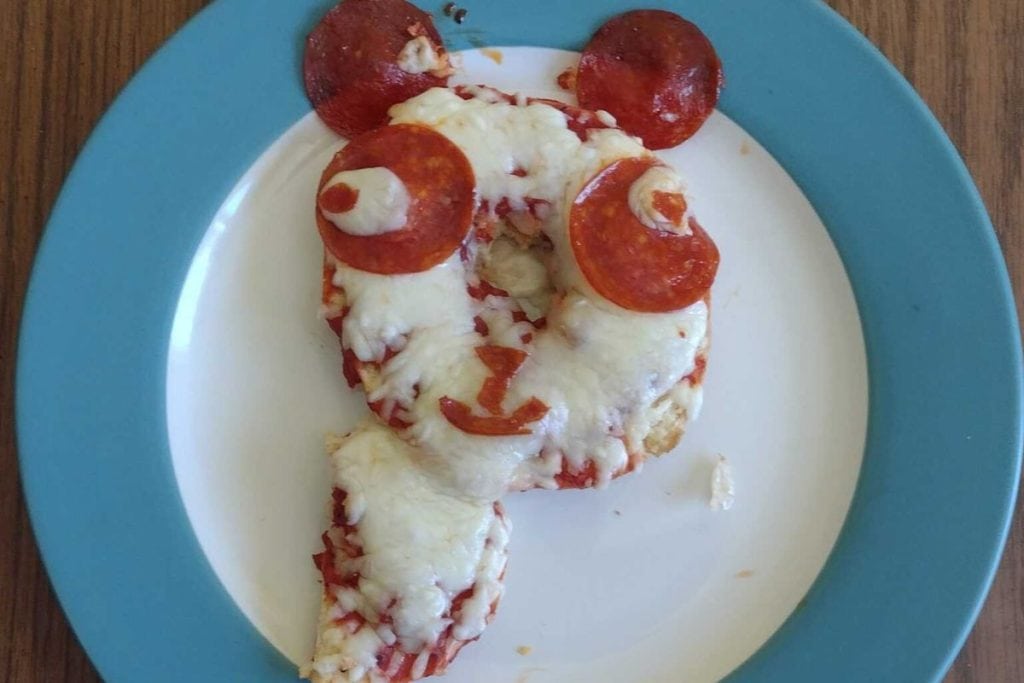 Bagel pizza shaped like a panda face with melted cheese, pepperoni, and sauce on a white plate with a blue rim.
